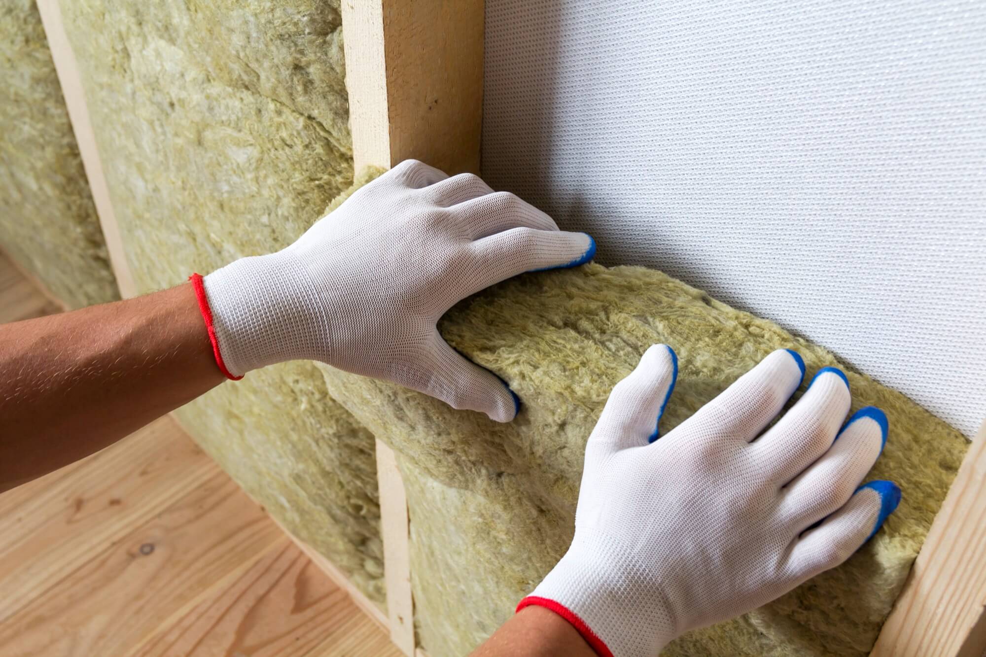 Close-up of a person wearing gloves installing mineral wool in a wooden stud wall for insulation.
